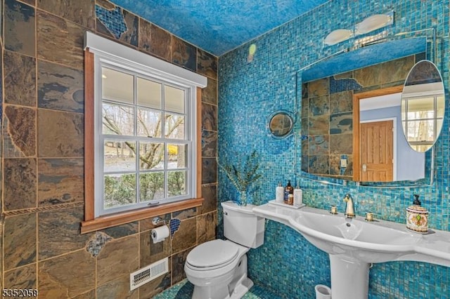 bathroom featuring toilet, visible vents, and tile walls