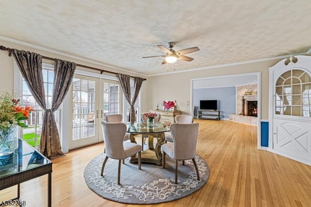 dining room with a warm lit fireplace, a ceiling fan, french doors, and light wood-type flooring