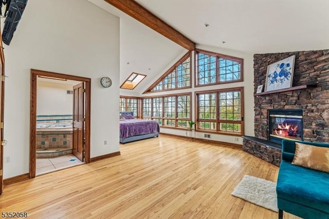 unfurnished bedroom with a stone fireplace, wood finished floors, beamed ceiling, baseboards, and high vaulted ceiling