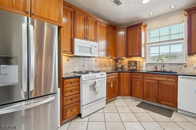 kitchen featuring white appliances, dark countertops, visible vents, and a sink