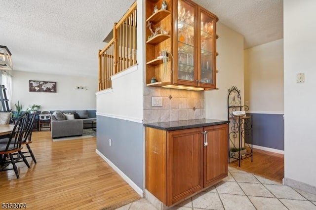 interior space with a textured ceiling, decorative backsplash, baseboards, and light wood finished floors