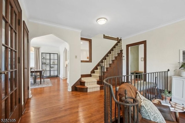 foyer entrance featuring crown molding, arched walkways, baseboards, and wood finished floors