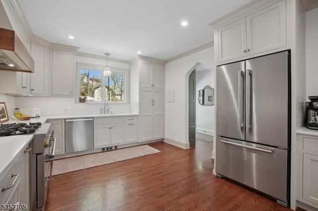 kitchen with a sink, arched walkways, wall chimney exhaust hood, stainless steel appliances, and dark wood-style floors