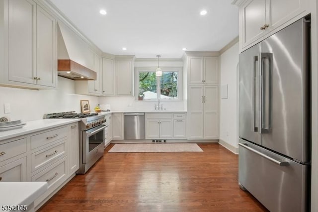 kitchen with crown molding, high end appliances, hanging light fixtures, wood finished floors, and light countertops