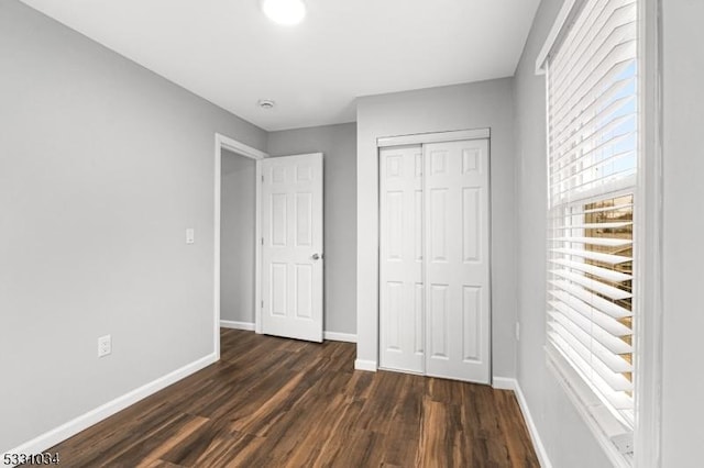 unfurnished bedroom featuring baseboards, a closet, and dark wood finished floors