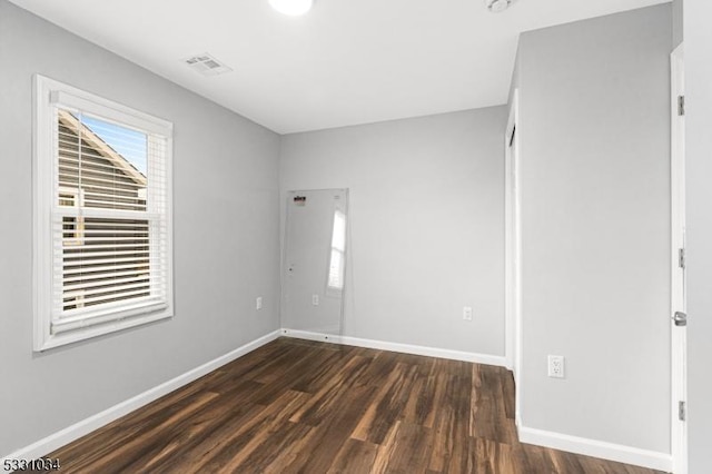 unfurnished room featuring visible vents, baseboards, and dark wood-type flooring