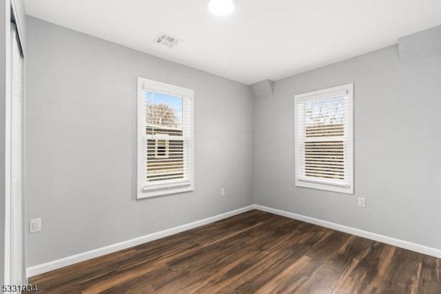 spare room with baseboards, visible vents, a wealth of natural light, and dark wood-style floors
