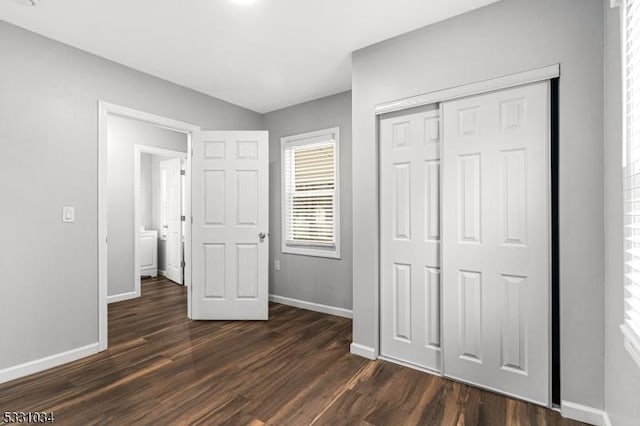 unfurnished bedroom with dark wood finished floors, a closet, and baseboards