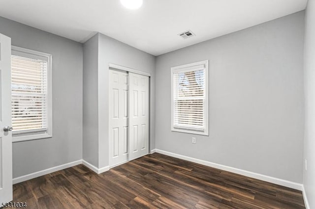 unfurnished bedroom with dark wood-type flooring, a closet, visible vents, and baseboards