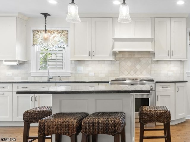 kitchen featuring stainless steel electric range, a sink, a breakfast bar area, light wood-style flooring, and white cabinetry