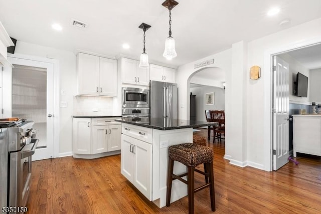 kitchen with visible vents, dark countertops, a kitchen breakfast bar, arched walkways, and appliances with stainless steel finishes