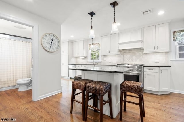 kitchen with a kitchen breakfast bar, visible vents, dark countertops, premium range hood, and baseboards