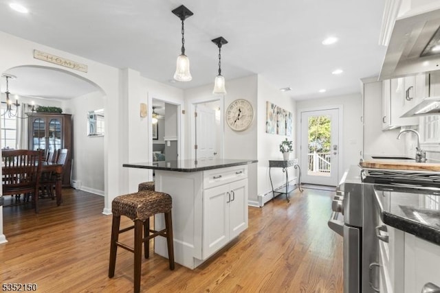 kitchen with gas range, arched walkways, range hood, a sink, and light wood finished floors