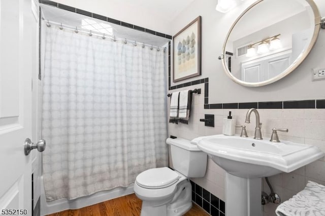 bathroom with wood finished floors, shower / bath combo, toilet, and tile walls