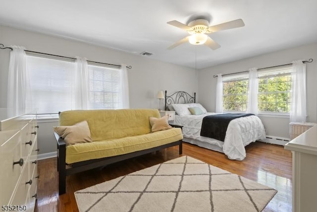 bedroom featuring a ceiling fan, visible vents, wood finished floors, baseboards, and a baseboard radiator