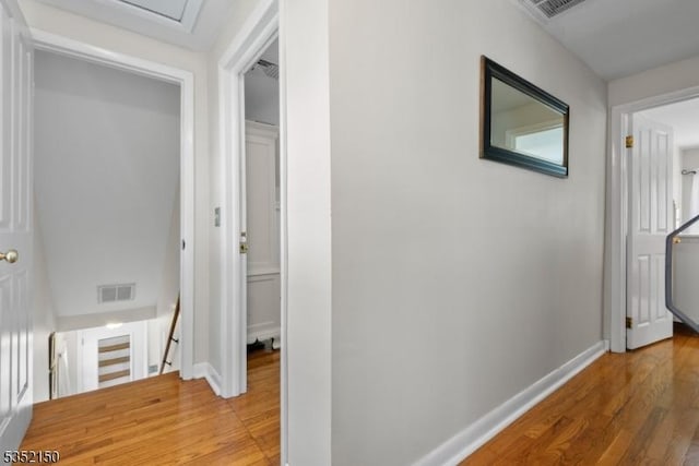 corridor with baseboards, visible vents, light wood-style flooring, and an upstairs landing