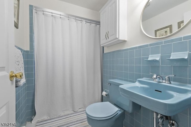 full bathroom with tile walls, wainscoting, curtained shower, a sink, and toilet