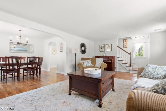 living area featuring arched walkways, wood finished floors, stairway, baseboards, and a notable chandelier