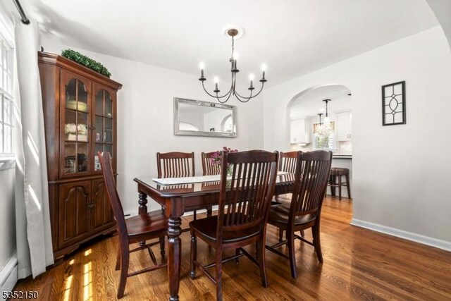 dining space with an inviting chandelier, arched walkways, baseboards, and wood finished floors