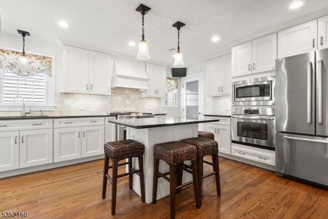 kitchen with white cabinets, appliances with stainless steel finishes, custom exhaust hood, and a sink