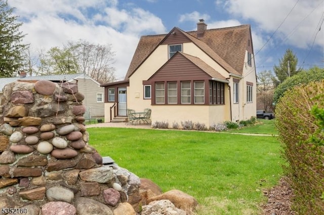 rear view of property with a chimney, entry steps, stucco siding, a lawn, and roof with shingles