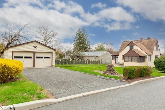 exterior space featuring an outbuilding, a detached garage, a chimney, fence, and a front yard