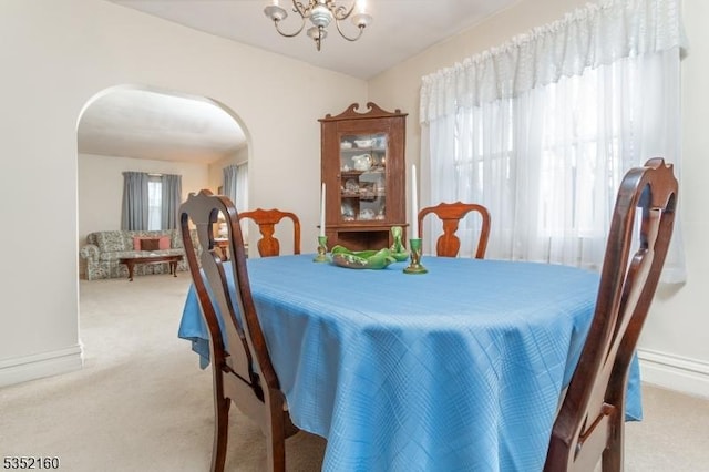 dining area with arched walkways, light carpet, a chandelier, and baseboards