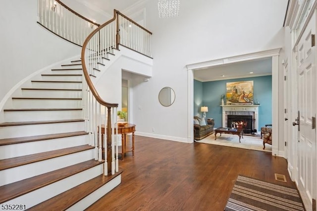foyer entrance featuring a towering ceiling, wood finished floors, a fireplace, stairs, and baseboards