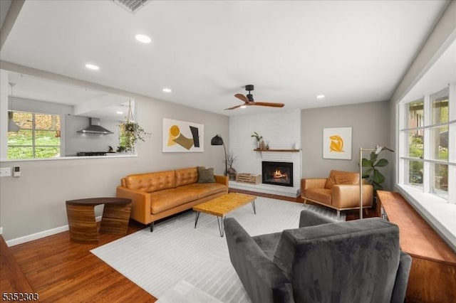 living area with wood finished floors, baseboards, ceiling fan, recessed lighting, and a large fireplace