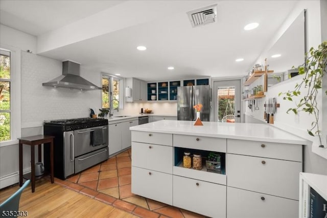 kitchen featuring wall chimney range hood, stainless steel appliances, visible vents, and a healthy amount of sunlight