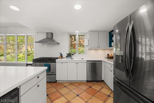 kitchen with light tile patterned flooring, appliances with stainless steel finishes, light countertops, wall chimney exhaust hood, and white cabinetry