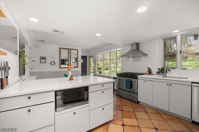 kitchen featuring recessed lighting, light countertops, wall chimney exhaust hood, white cabinets, and appliances with stainless steel finishes