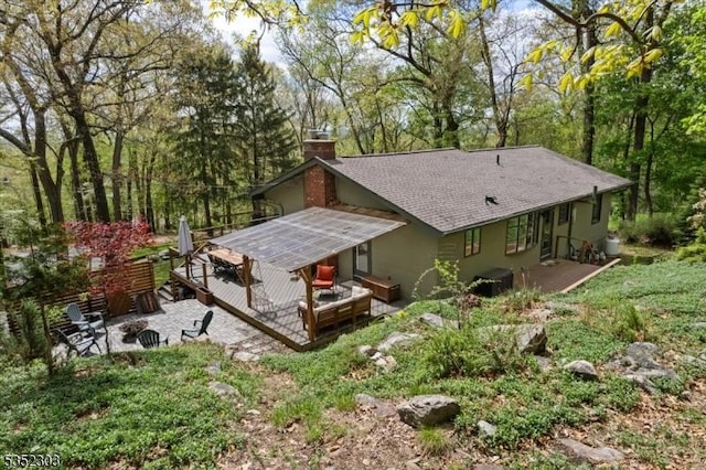 back of house featuring a chimney, roof with shingles, a wooden deck, an outdoor fire pit, and a patio