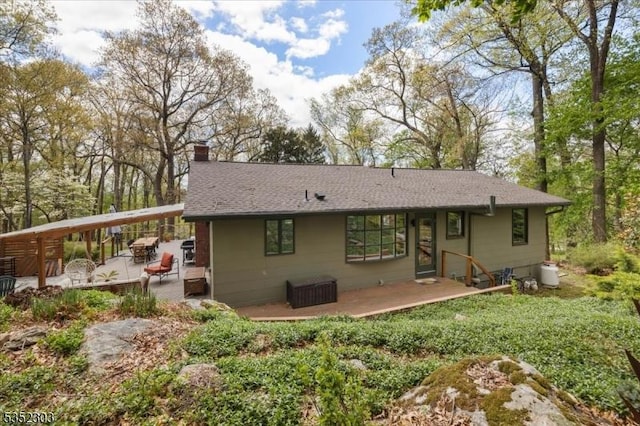 rear view of house featuring a deck, a chimney, and roof with shingles