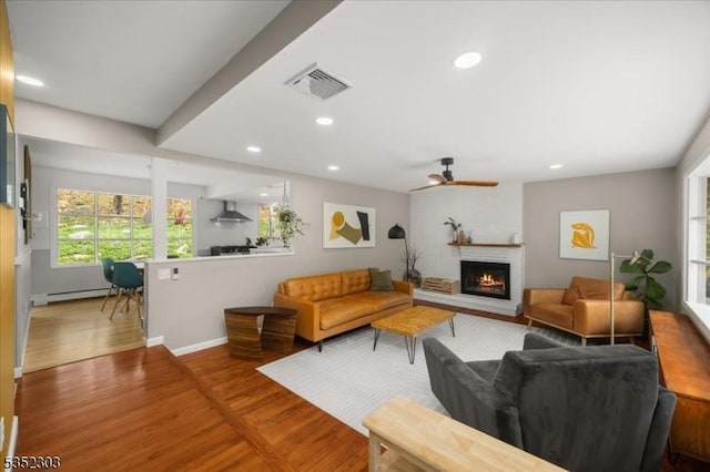 living room featuring visible vents, a baseboard heating unit, wood finished floors, and a large fireplace