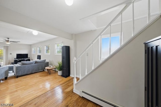 living room featuring stairway, a baseboard heating unit, wood finished floors, and a healthy amount of sunlight