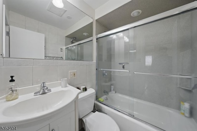 bathroom with vanity, decorative backsplash, toilet, shower / bath combination with glass door, and tile walls
