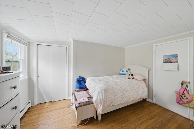 bedroom with light wood-type flooring, a baseboard radiator, and a closet
