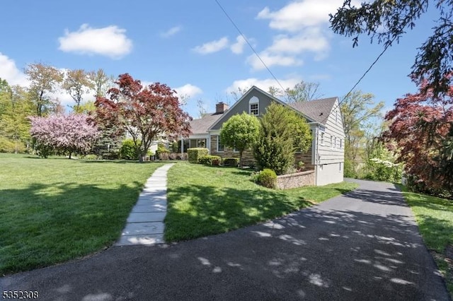 view of front of house featuring a chimney, a front lawn, and aphalt driveway