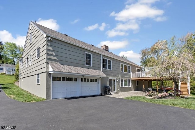 view of front facade with a garage, a deck, stairway, a chimney, and driveway