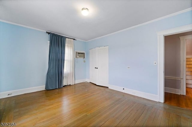 empty room featuring hardwood / wood-style flooring, an AC wall unit, crown molding, and baseboards