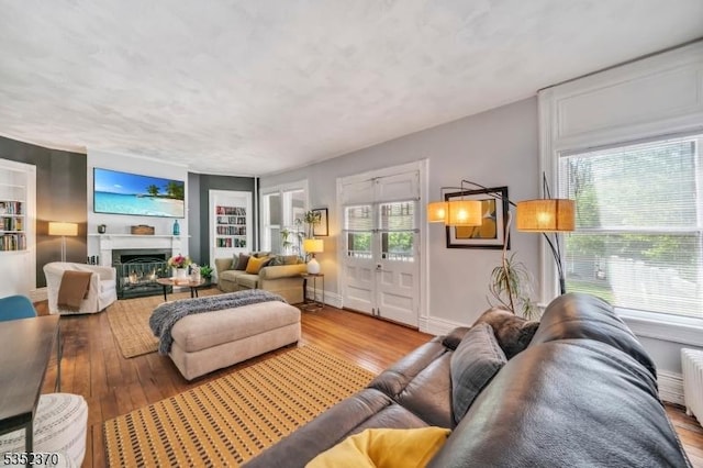 living room featuring built in features, a fireplace, wood finished floors, and a wealth of natural light