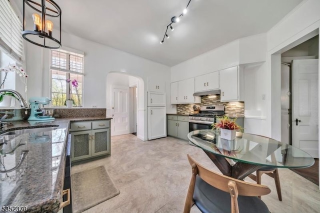 kitchen with gas range, arched walkways, tasteful backsplash, a sink, and under cabinet range hood