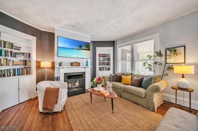living room featuring a fireplace with flush hearth, crown molding, wood-type flooring, and built in shelves