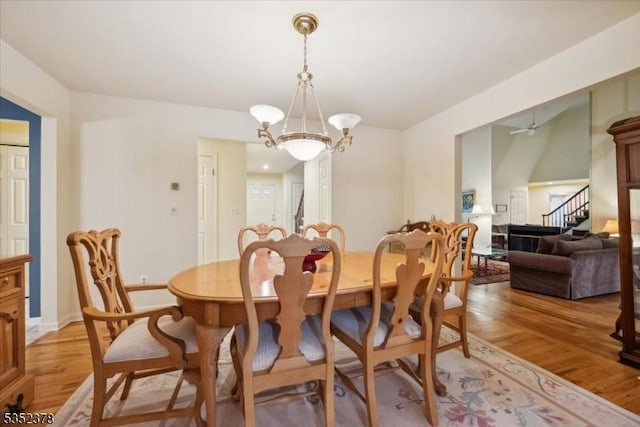 dining space with a chandelier, light wood finished floors, stairs, a ceiling fan, and baseboards