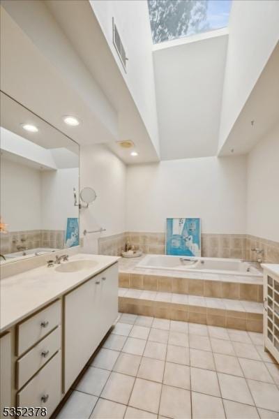 full bathroom featuring vanity, tile patterned floors, a garden tub, a towering ceiling, and a skylight