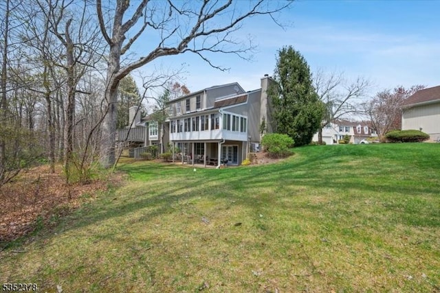 back of property with a chimney, a sunroom, a lawn, and a deck