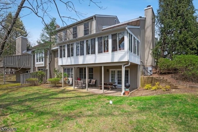 back of house with french doors, a chimney, a patio area, a sunroom, and a yard