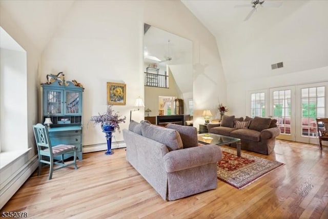 living area featuring ceiling fan, high vaulted ceiling, light wood-type flooring, and a baseboard radiator