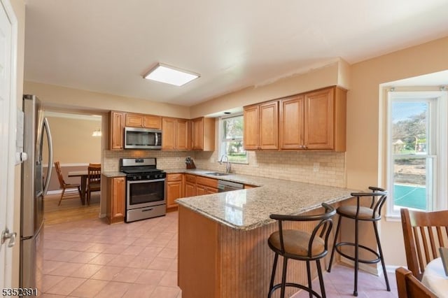 kitchen with light stone counters, decorative backsplash, light tile patterned floors, appliances with stainless steel finishes, and a peninsula